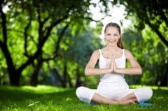 Woman sitting cross-legged outdoors, meditating in a forest clearing