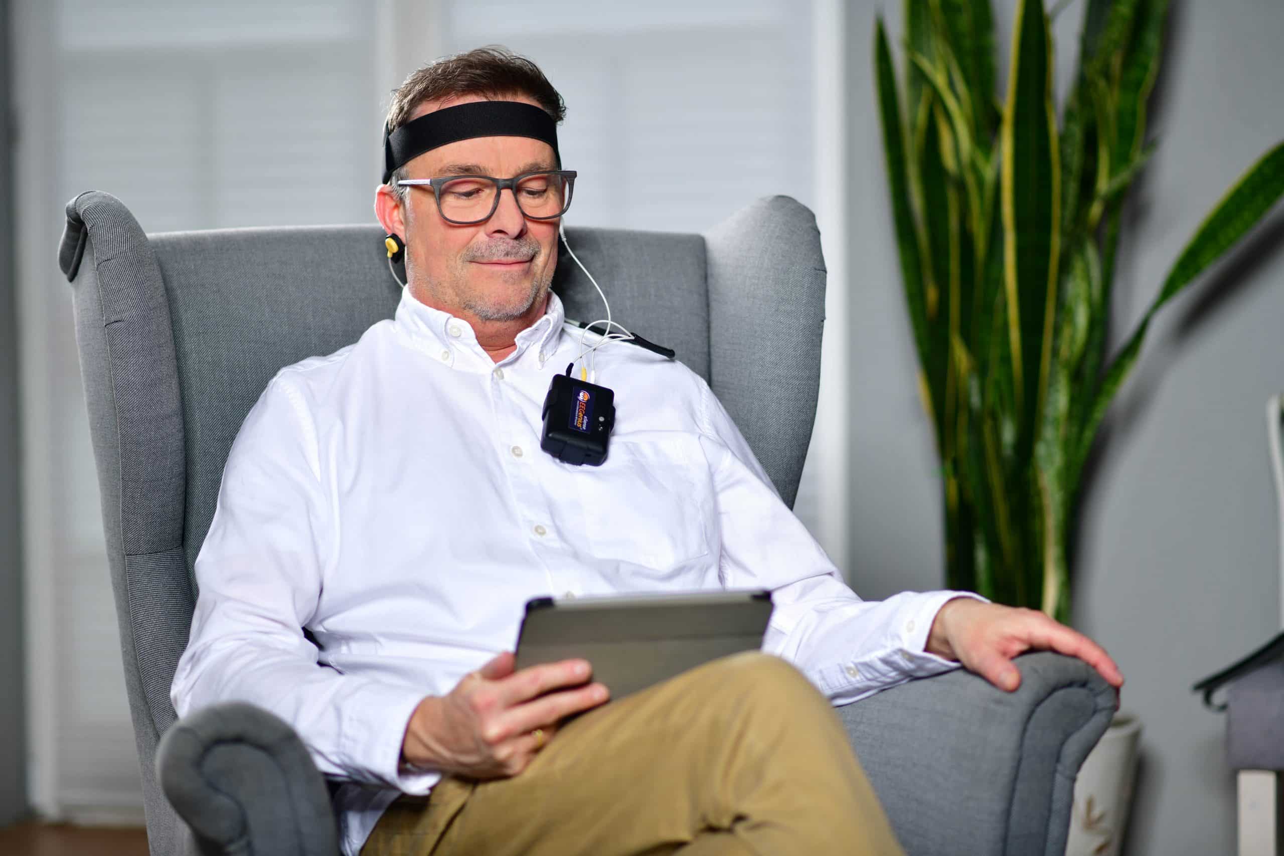 Mann mit Mindfield eSense EEGenius Stirnband und Sensor sitzt entspannt mit Tablet im Sessel