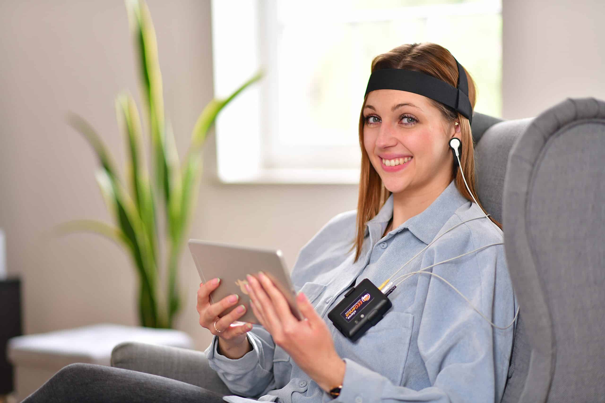 Frau mit eSense-EEGenius-Stirnband sitzt entspannt mit Tablet im Sessel