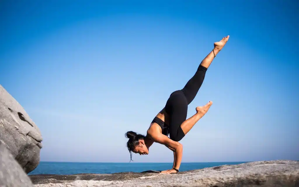 Frau in Yoga-Haltung auf Felsen am Meer
