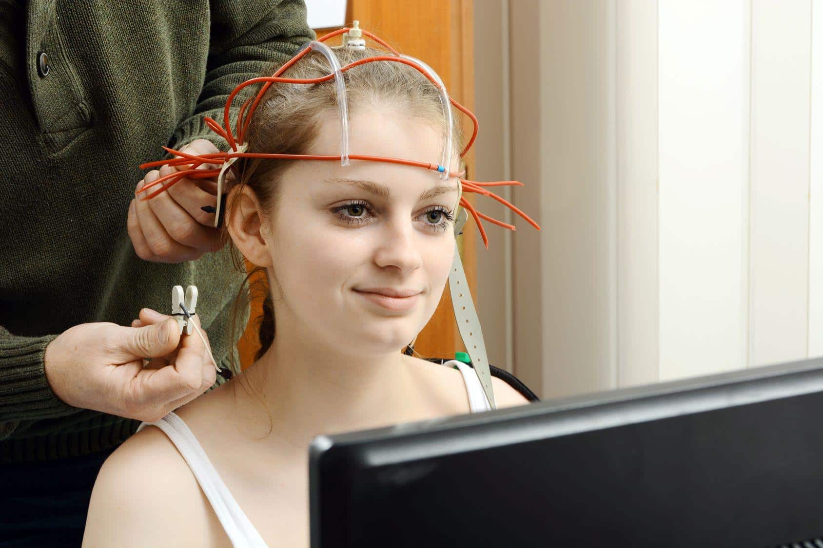 Biofeedback Einer Frau wird vor einem Monitor eine EEG-Haube angelegt