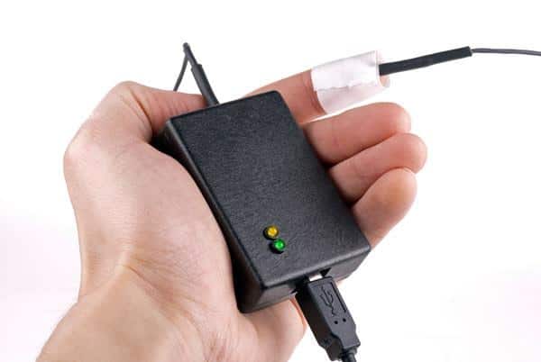 Hand holding the small black skin temperature sensor unit with attached probe